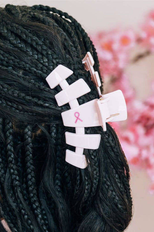 Hair clip with pink ribbon on braided hair against a blurred floral background